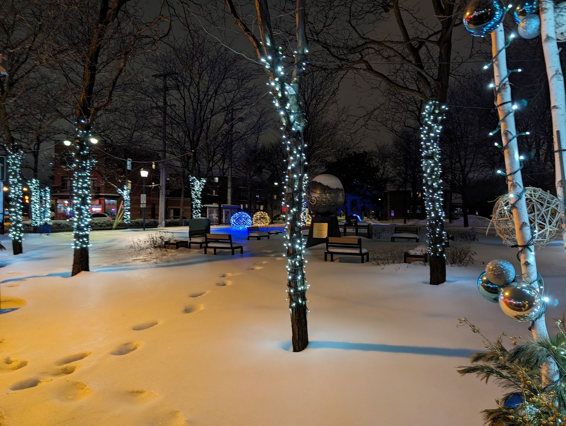 A park covered in snow at night with christmas lights on the trees.