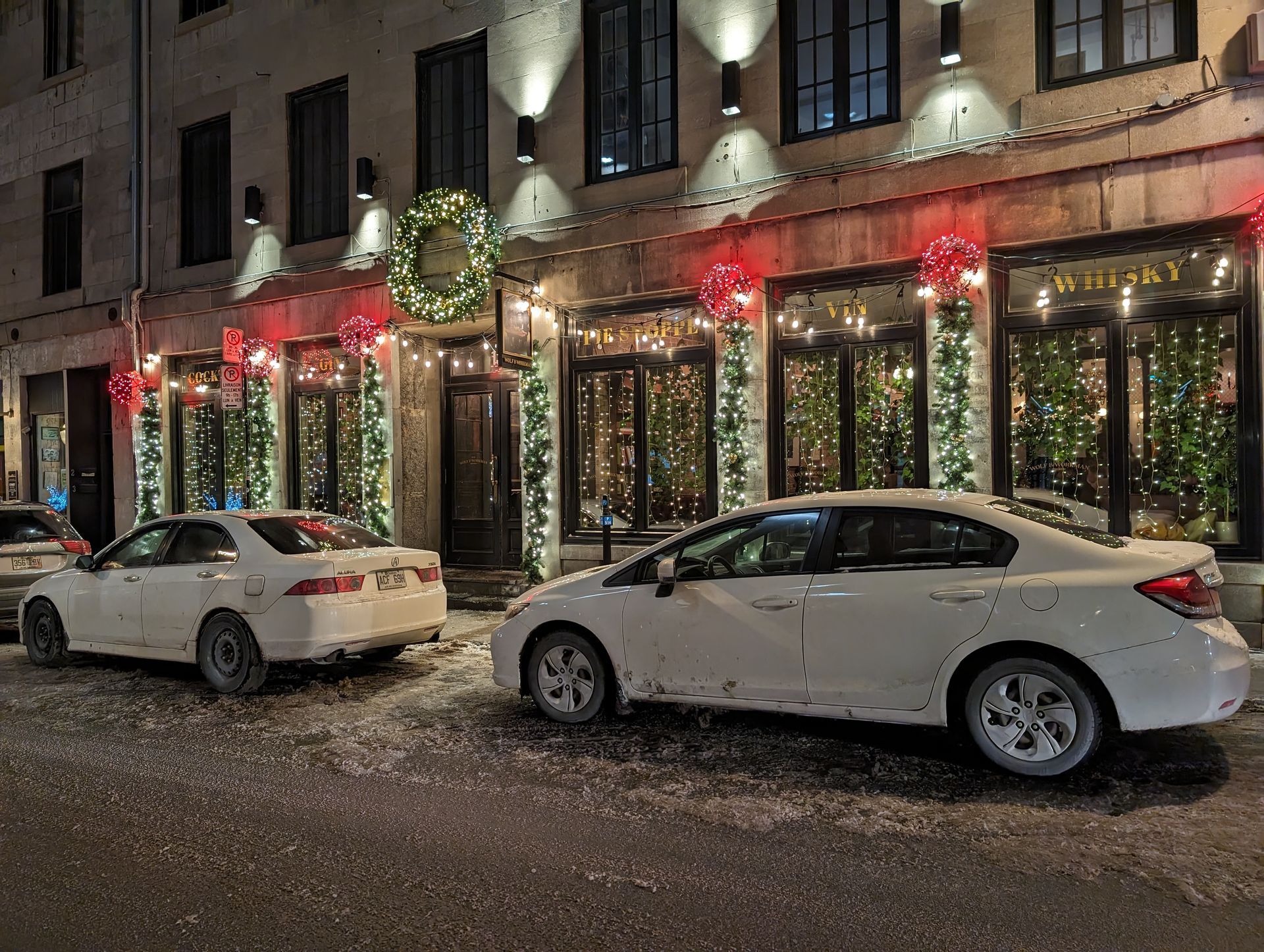 Deux voitures blanches sont garées devant un bâtiment décoré pour Noël.