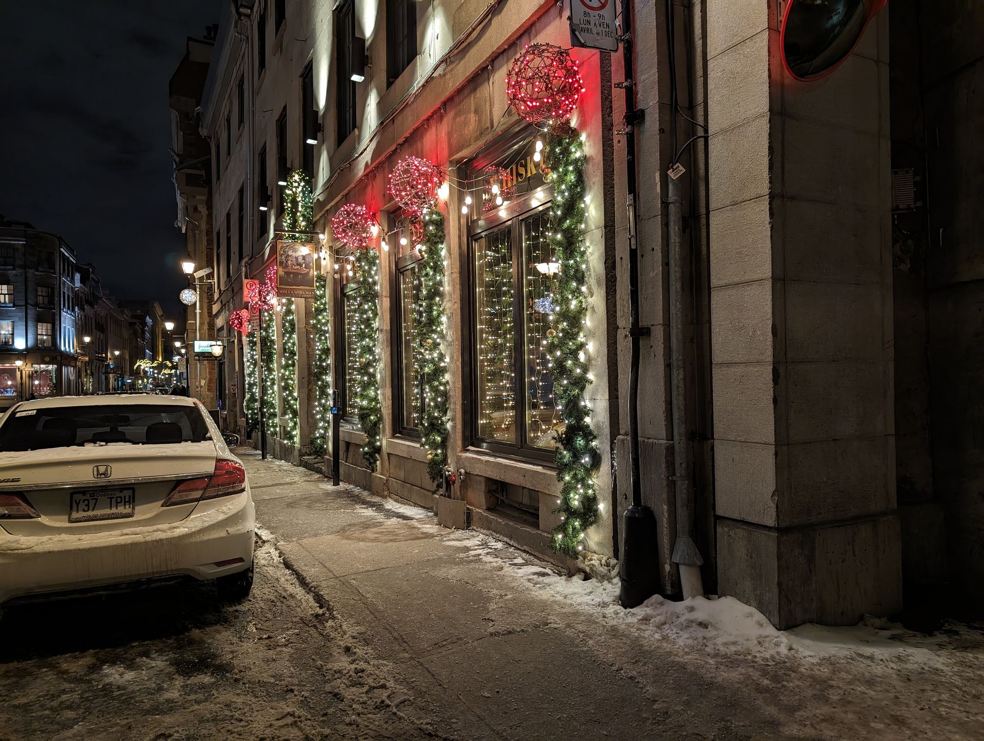 A white car is parked in front of a building decorated for christmas.