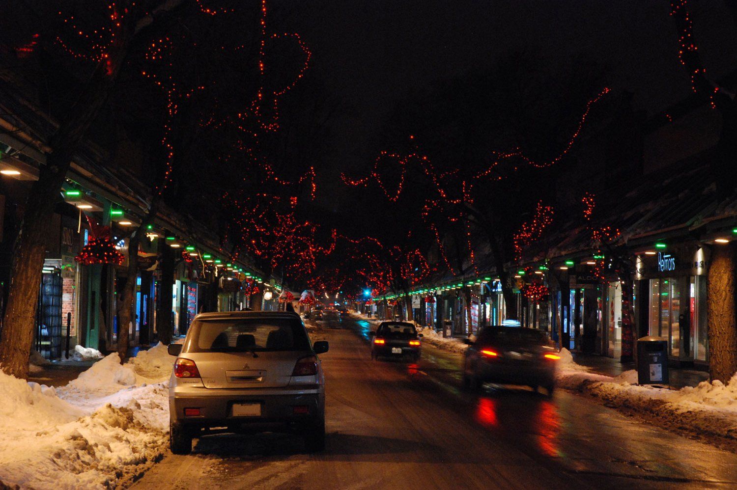 Une voiture est garée sur le bord d'une rue enneigée la nuit.