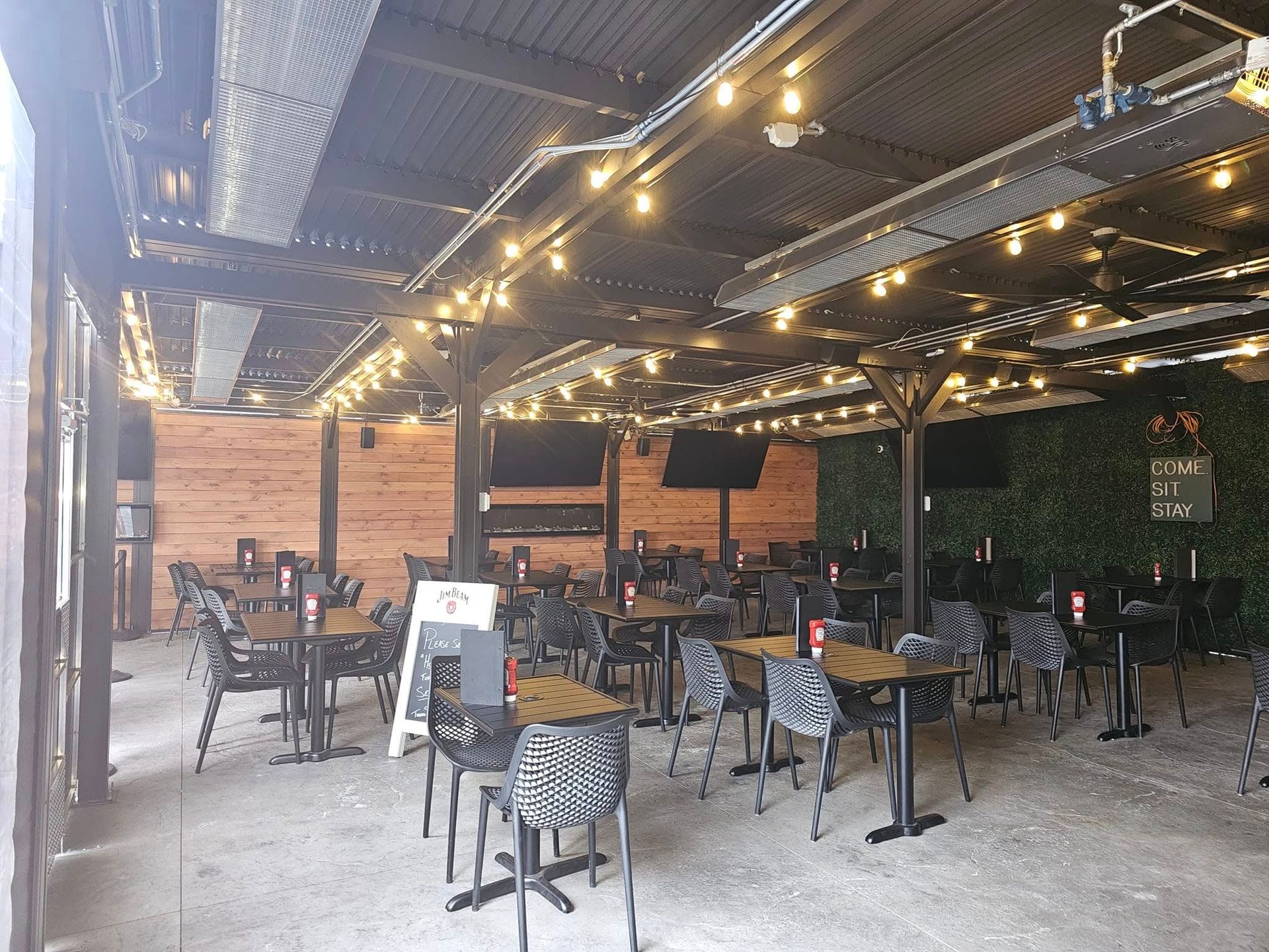 Outdoor restaurant seating area with tables, chairs, string lights, and a wooden ceiling.