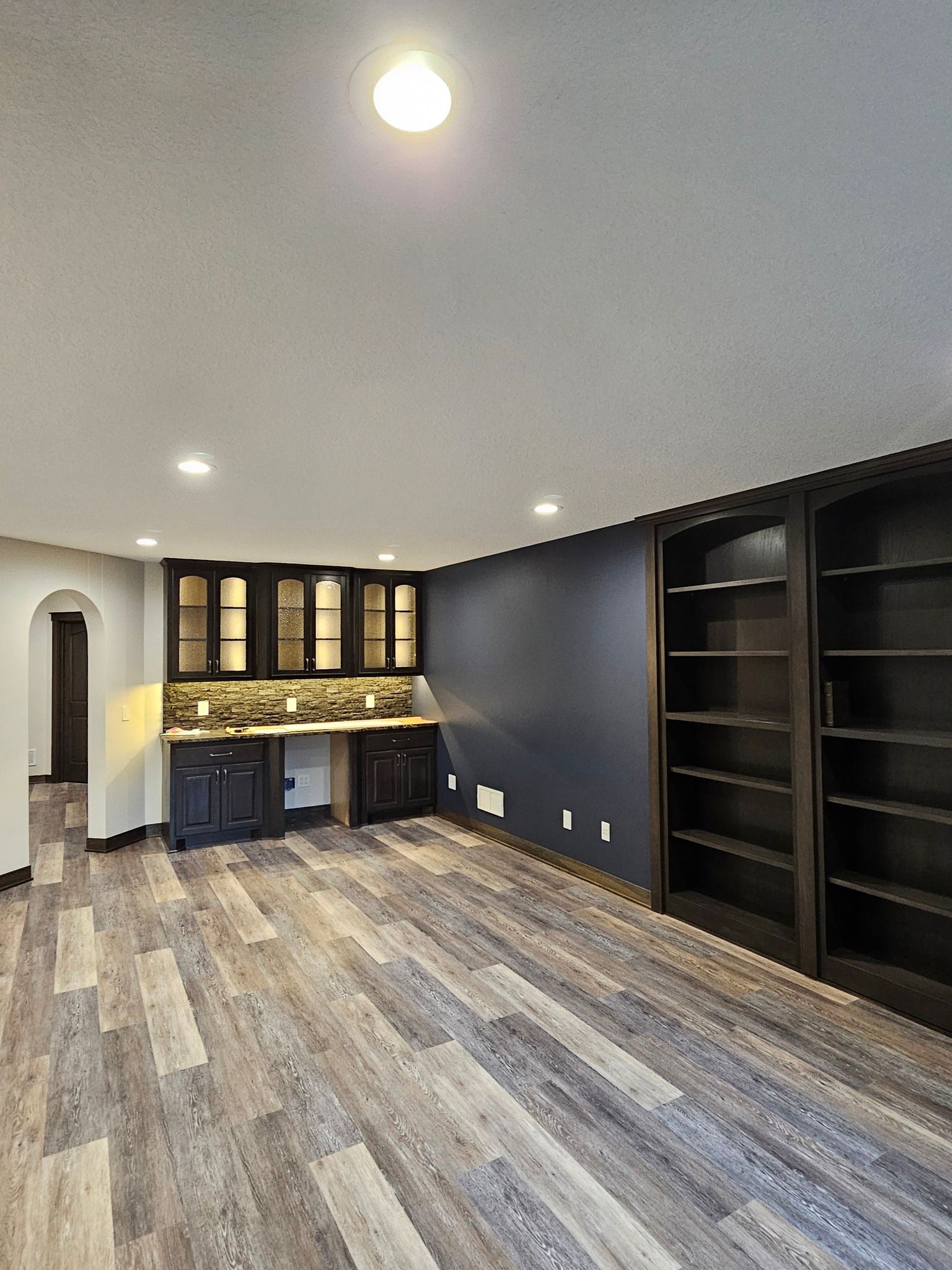 Interior room with dark wood cabinets, built-in shelving, blue accent wall, and wood-look flooring.