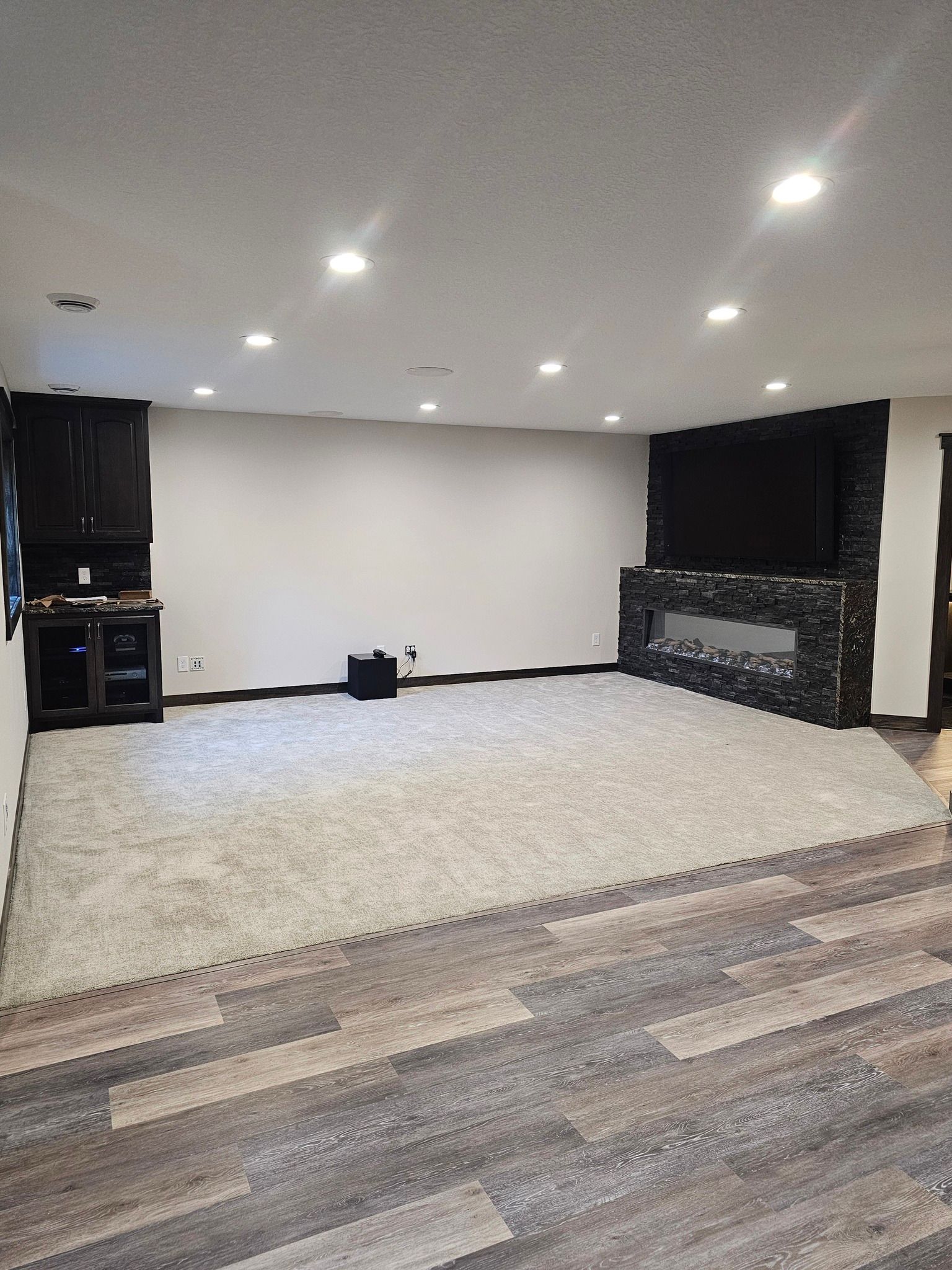 Empty finished basement with gray walls, fireplace, TV, and light carpet over wood-look flooring.