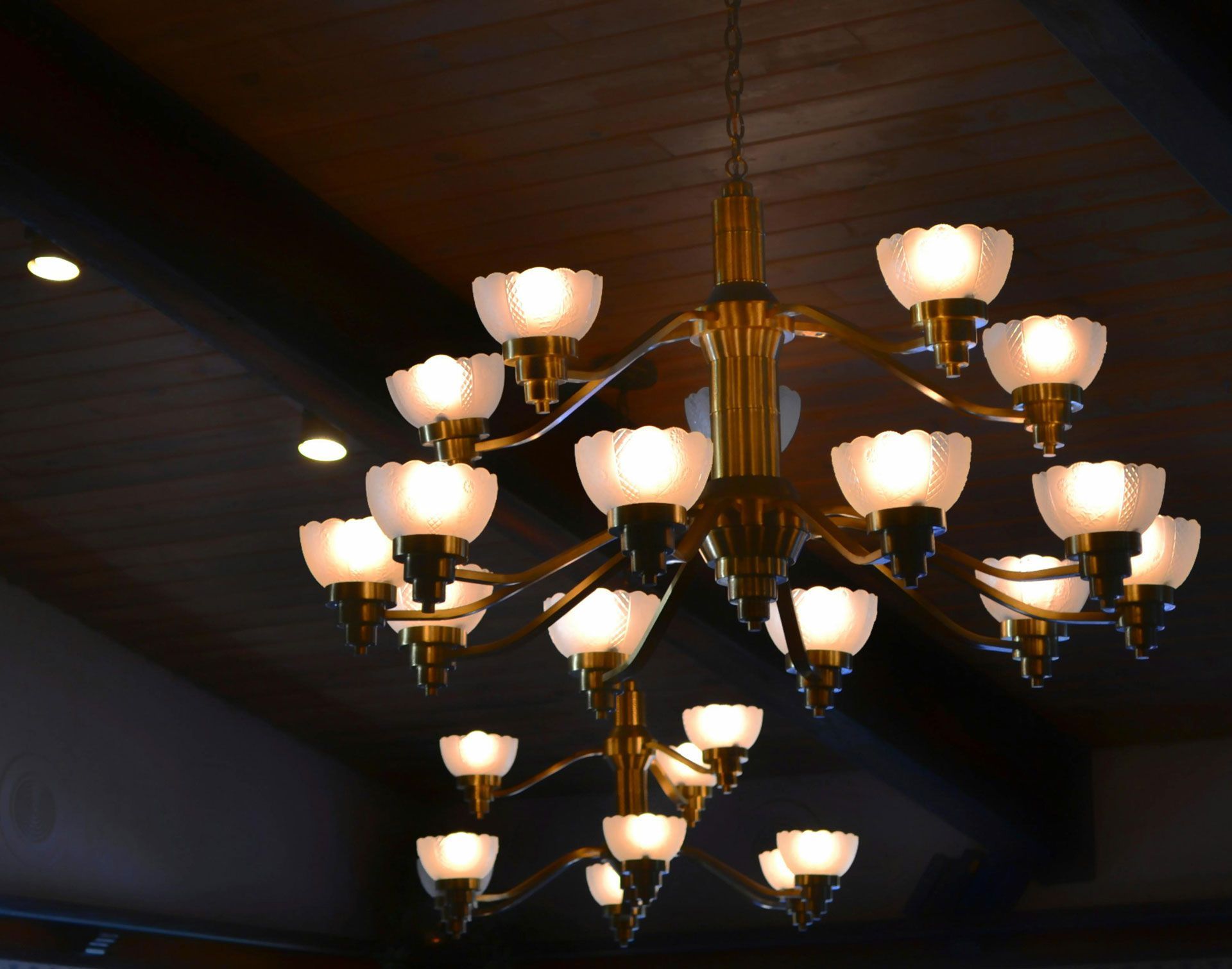 Ornate brass chandelier with frosted glass shades, hanging from a dark wooden ceiling.