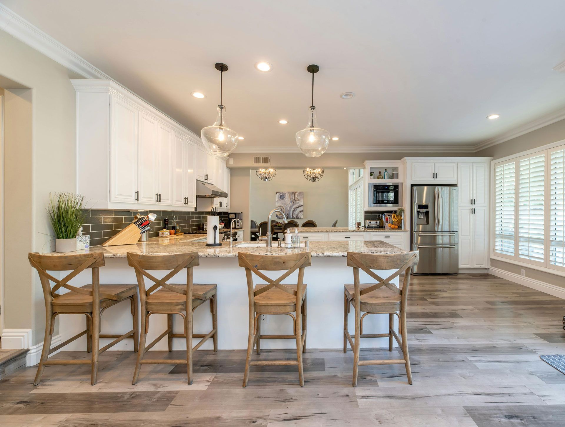 Kitchen with white cabinets, island with stools, stainless steel appliances, and wood flooring.