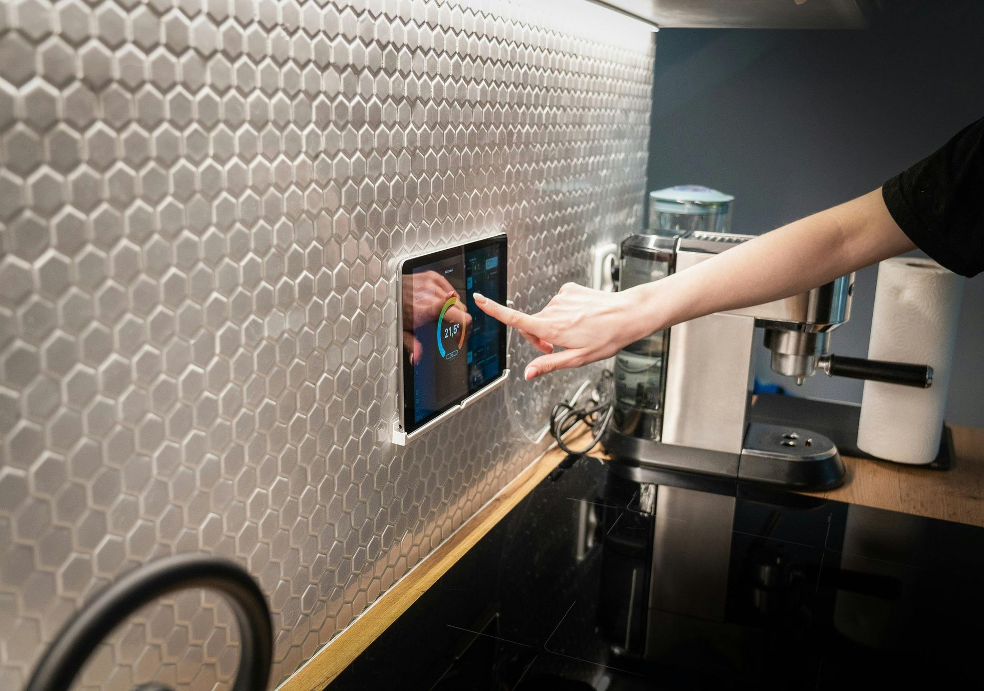 A person's hand touching a tablet embedded in a tiled kitchen wall.