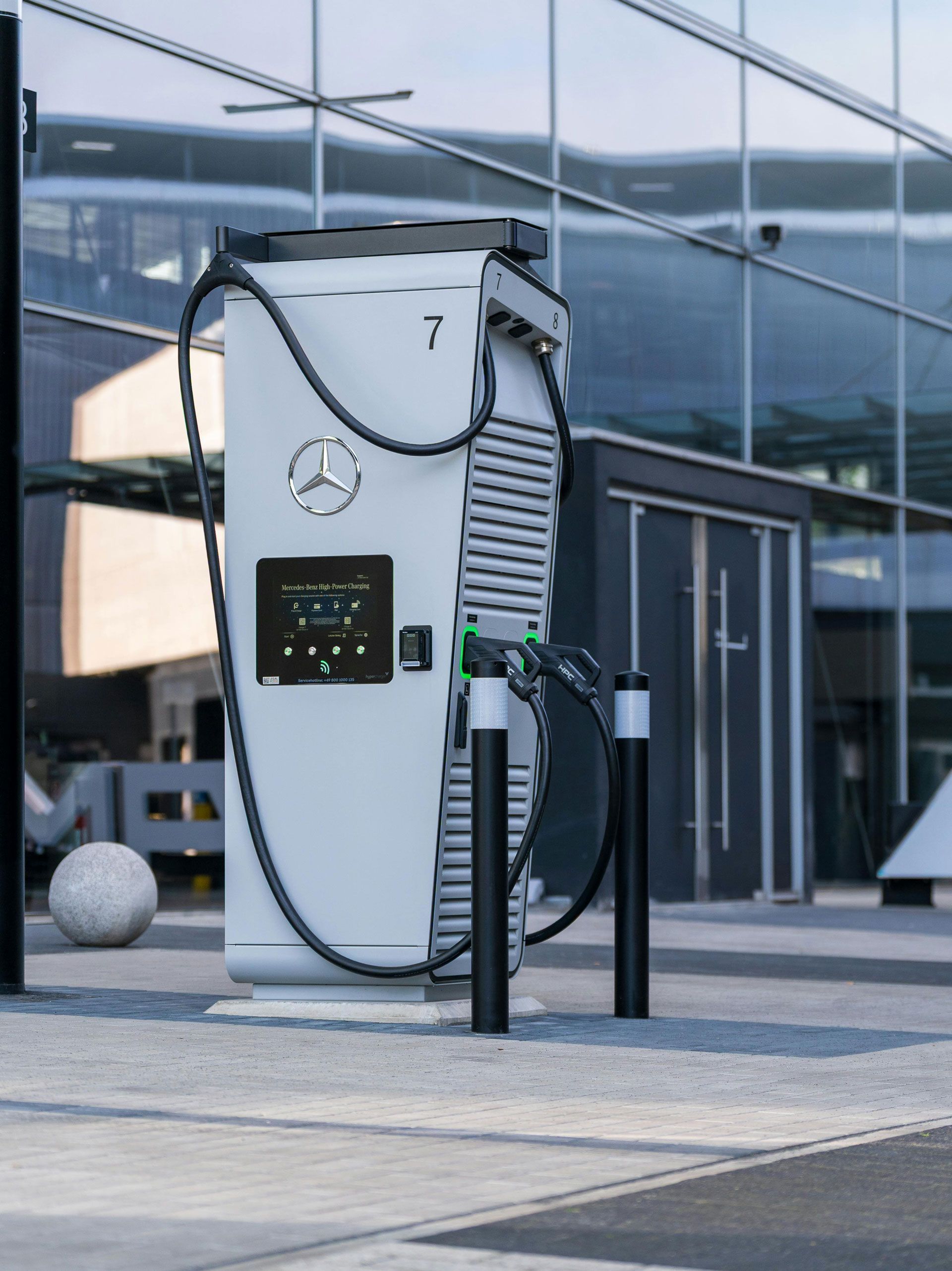 White Mercedes-Benz electric vehicle charging station with two black posts in front of a modern building.
