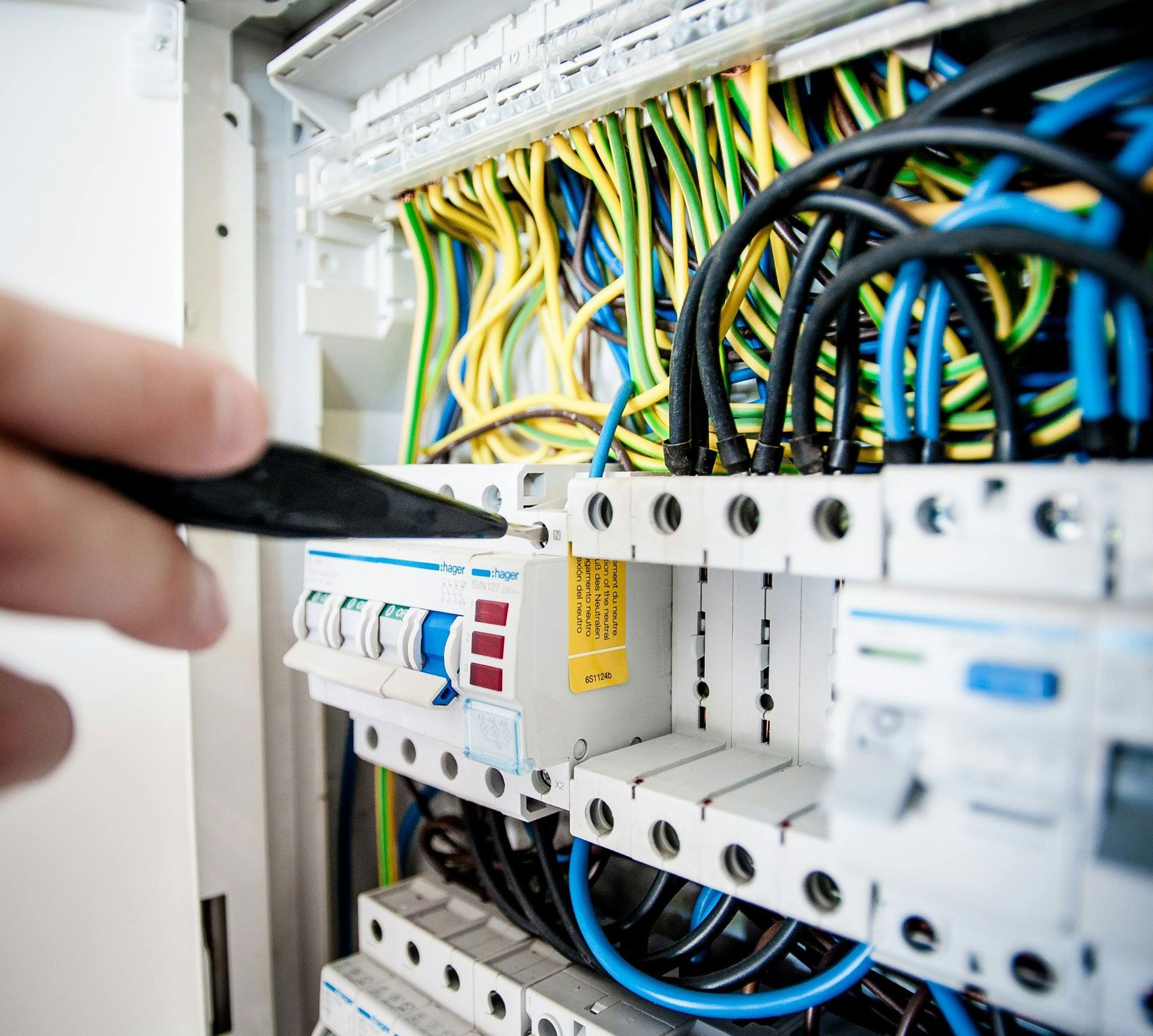 Electrician working on a fuse box, using a tool. Wires of various colors are visible.