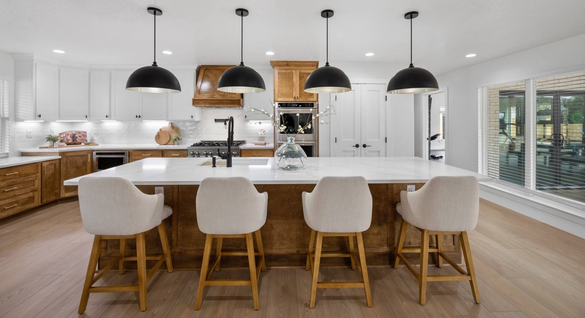 Bright modern kitchen with white cabinets, wood island, and four white bar stools beneath black pendant lights