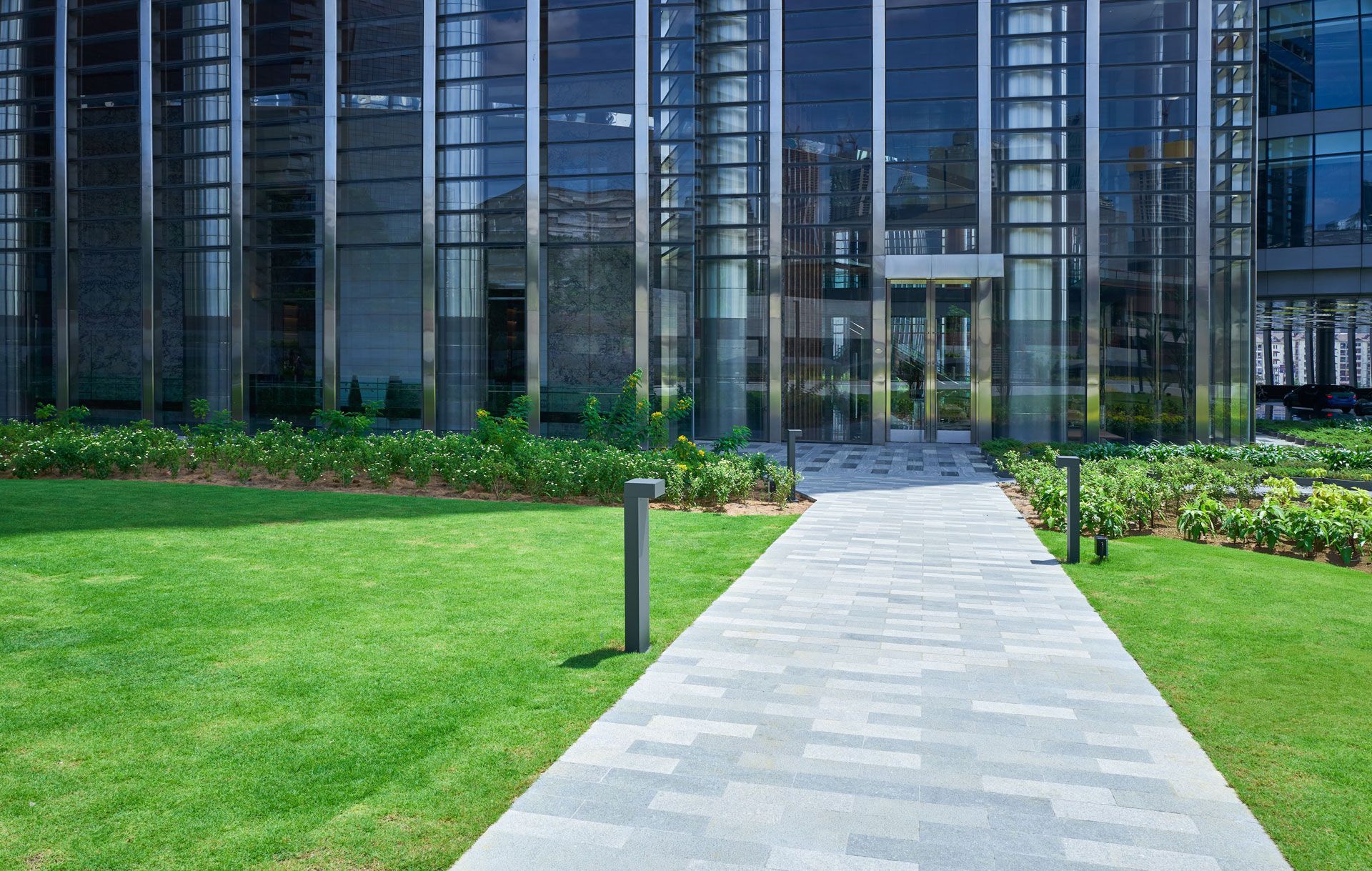 Modern glass office building with a paved walkway and green lawn in front