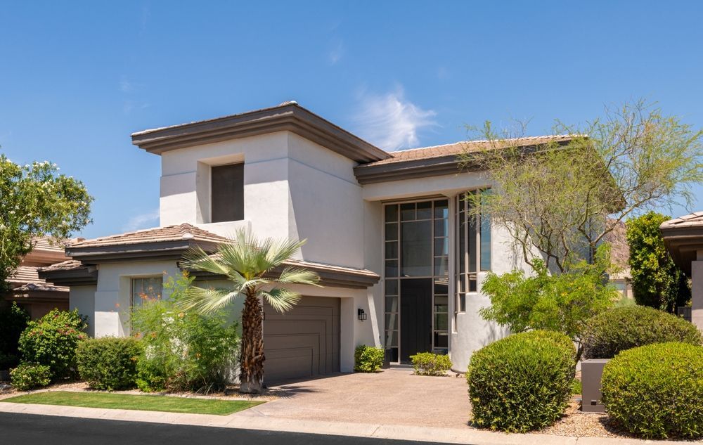 Modern two-story stucco house with garage, palm tree, and desert landscaping under a clear blue sky