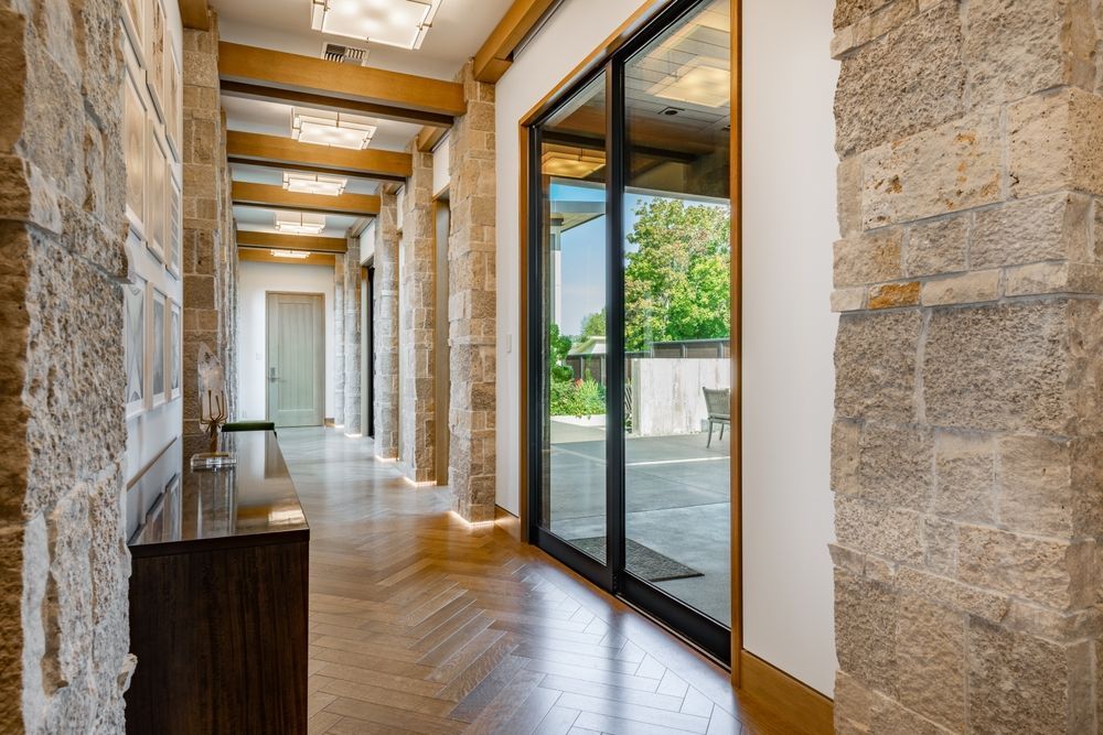Stone hallway with exposed beams, wood floor, and glass doors opening to a bright outdoor terrace