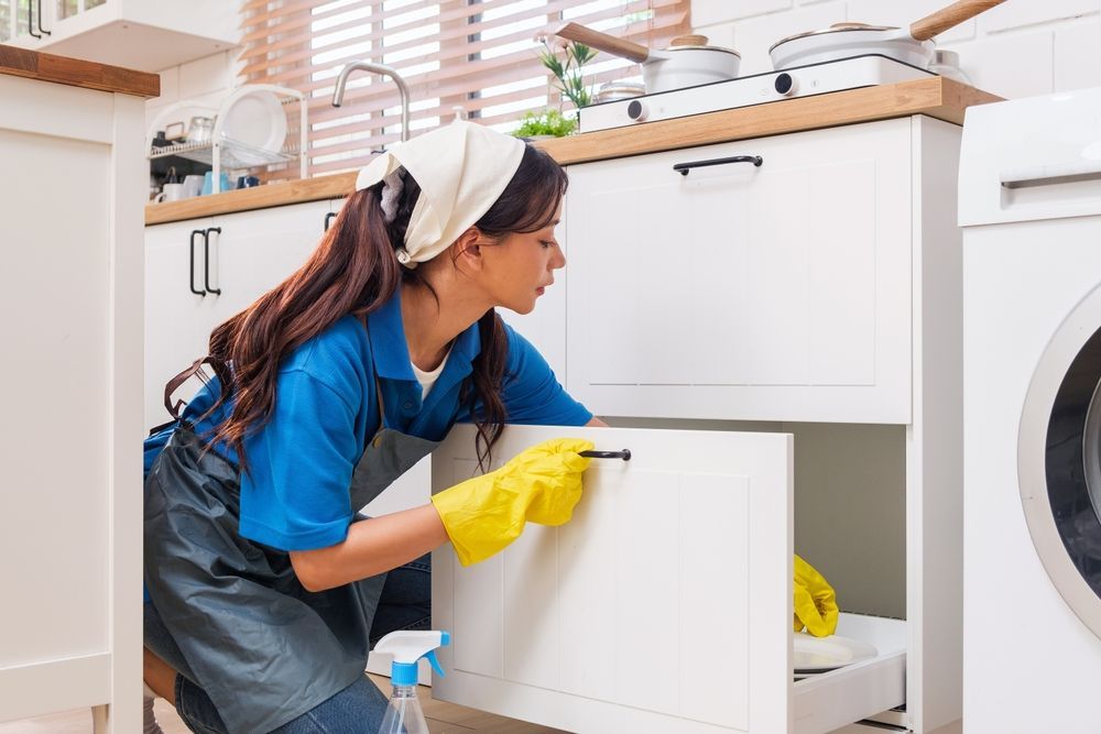 Person in blue shirt and yellow gloves loading a dishwasher in a bright kitchen
