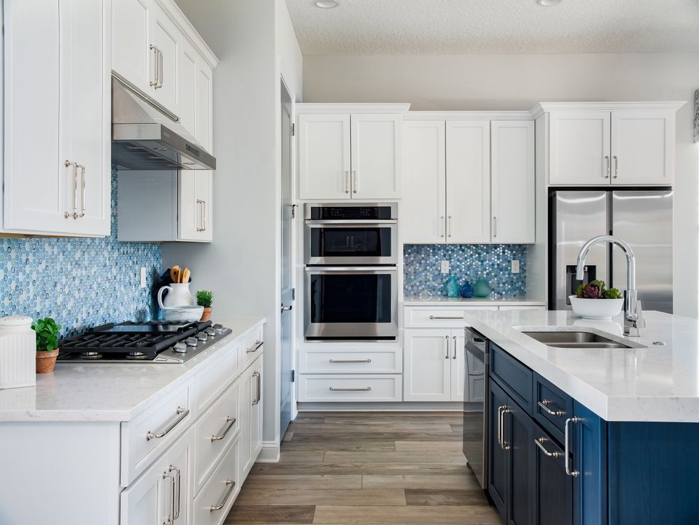 Bright modern kitchen with white cabinets, blue island, stainless appliances, and mosaic backsplash