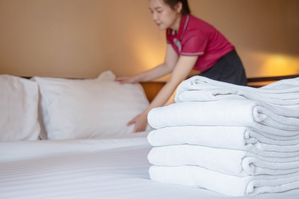 Housekeeper making a bed with folded white towels in a hotel room