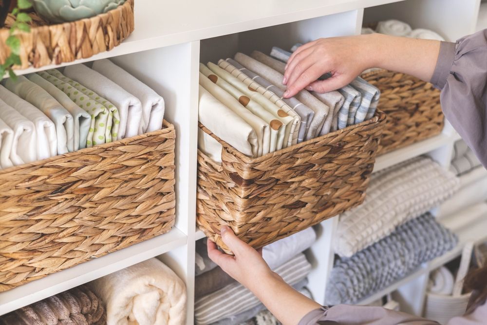 Hands organizing folded towels in woven baskets on white shelves