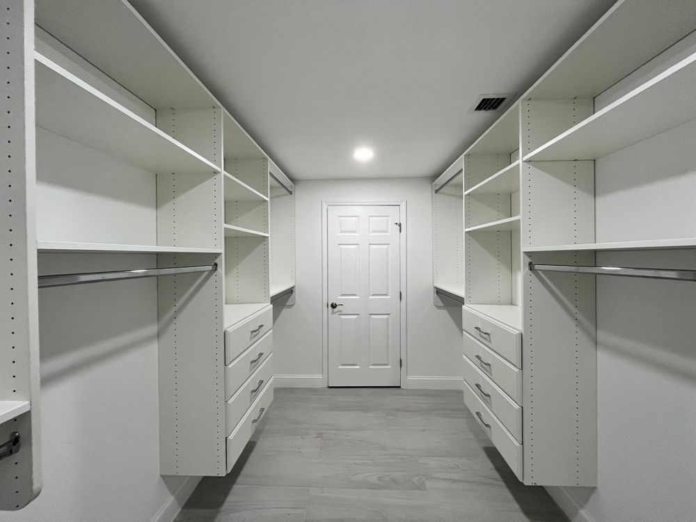 Walk-in closet with white shelving and drawers on both sides, centered on a closed white door.