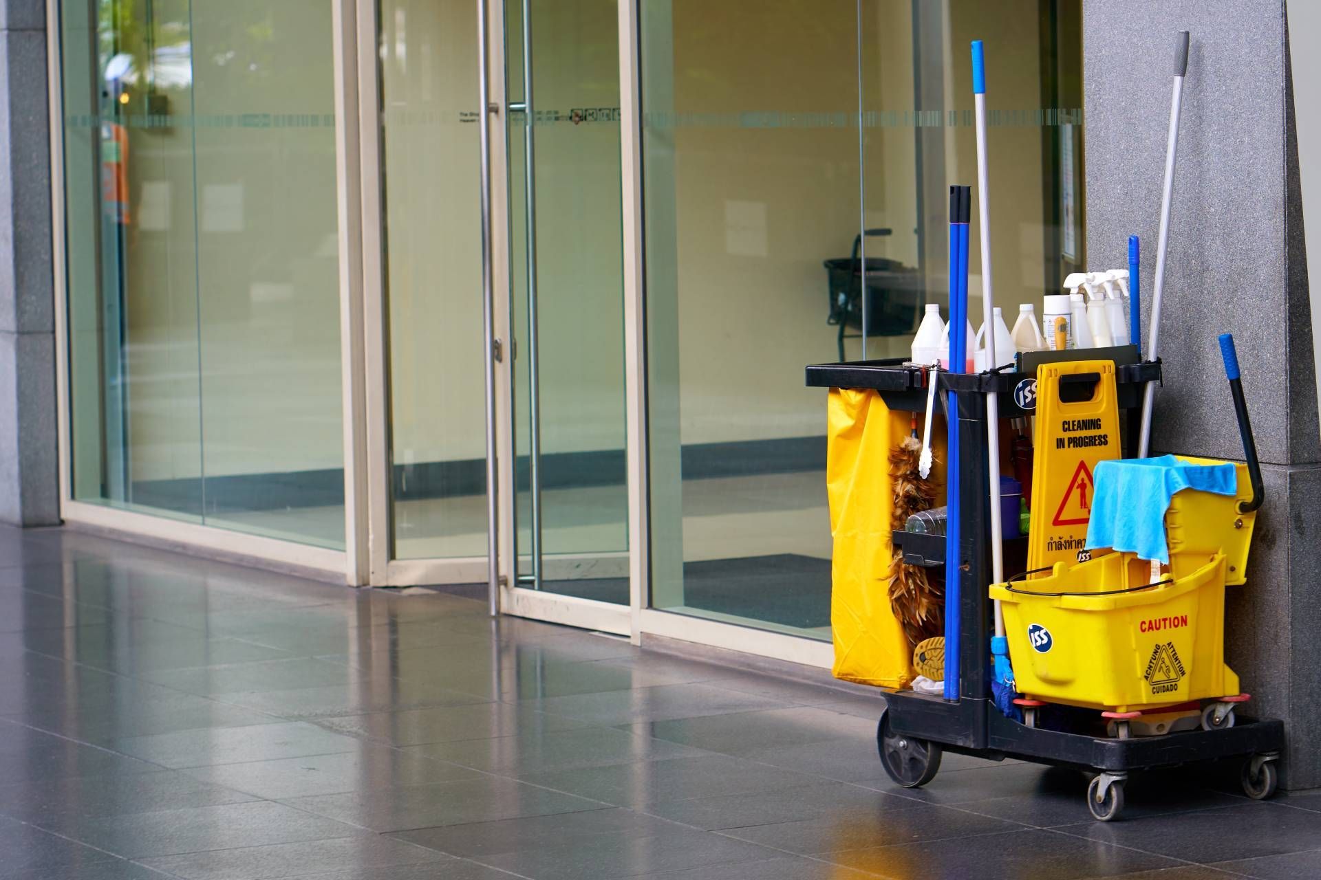 Yellow cleaning cart with supplies beside a glass building entrance