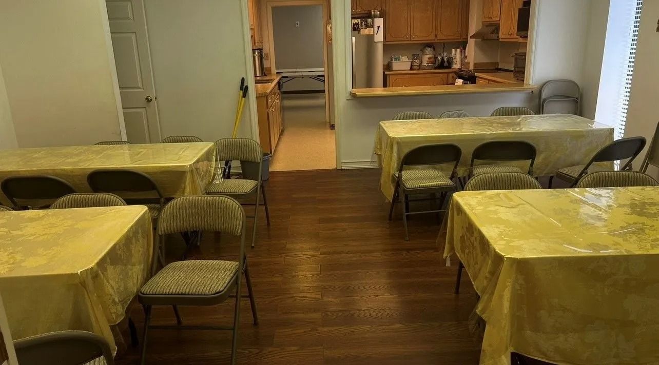 Empty dining room with yellow tablecloths, wooden floor, and a small kitchen pass-through in back