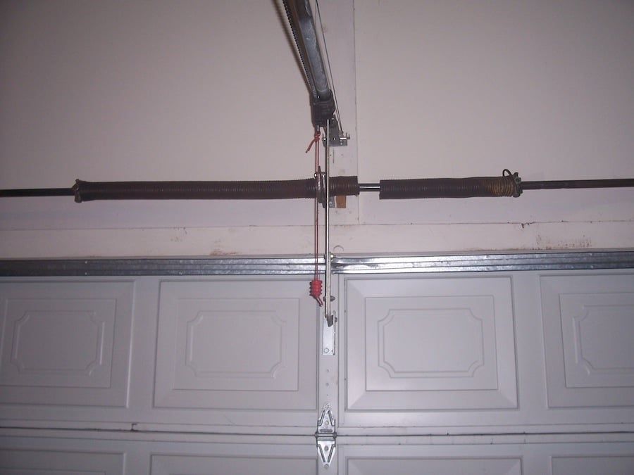 Interior view of garage door mechanism with visible rail, chain, and tensioned springs.