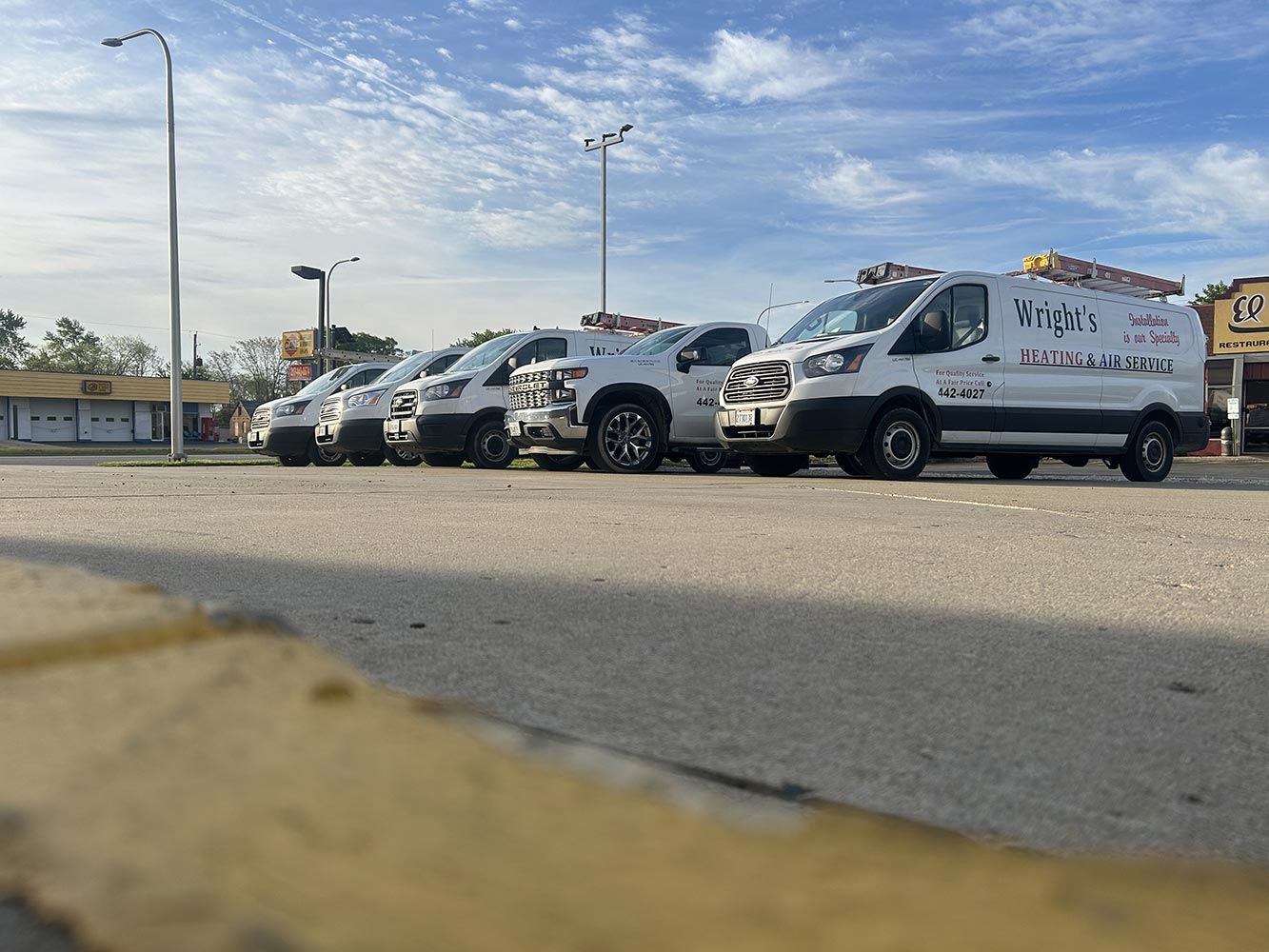 A row of white vans are parked in a parking lot.