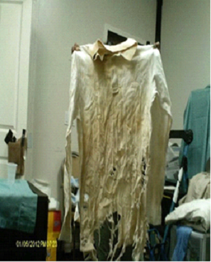 A tattered, stained white shirt with a tan collar hangs in a room with other clothing and furniture.