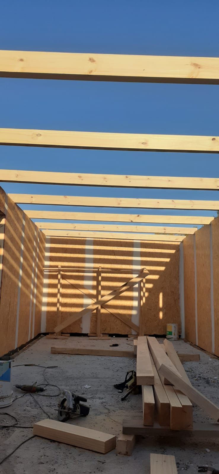Vista interior de un edificio en construcción. Vigas de madera y paredes sin terminar con herramientas.