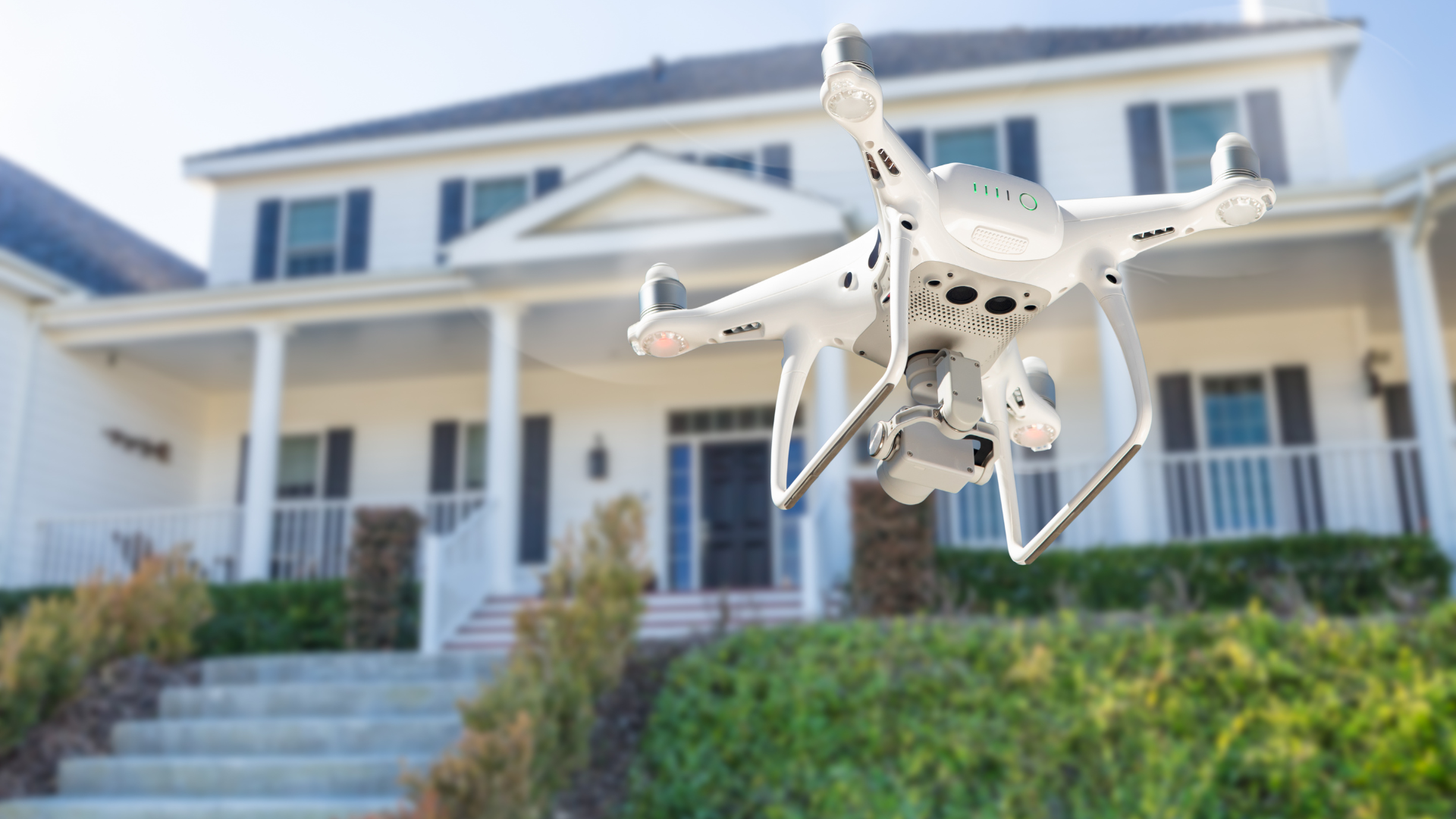 A drone is flying in front of a large white house.