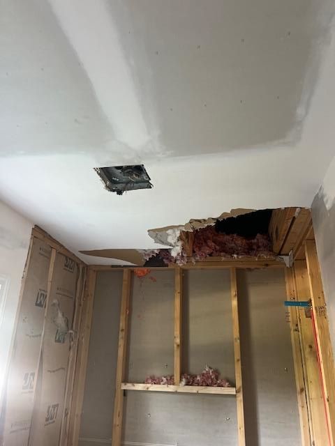 Ceiling with a large hole exposing wood framing and insulation. Wall studs are visible.