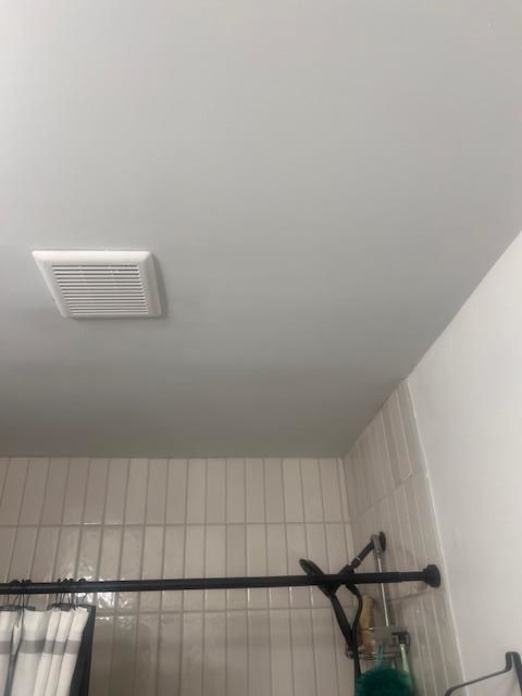 Bathroom ceiling with exhaust fan, white tiles and wall. Black shower rod.