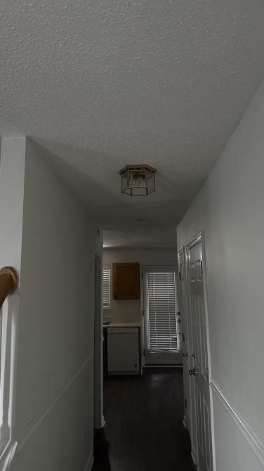 Narrow hallway with white walls, dark floor, and kitchen visible at the end.