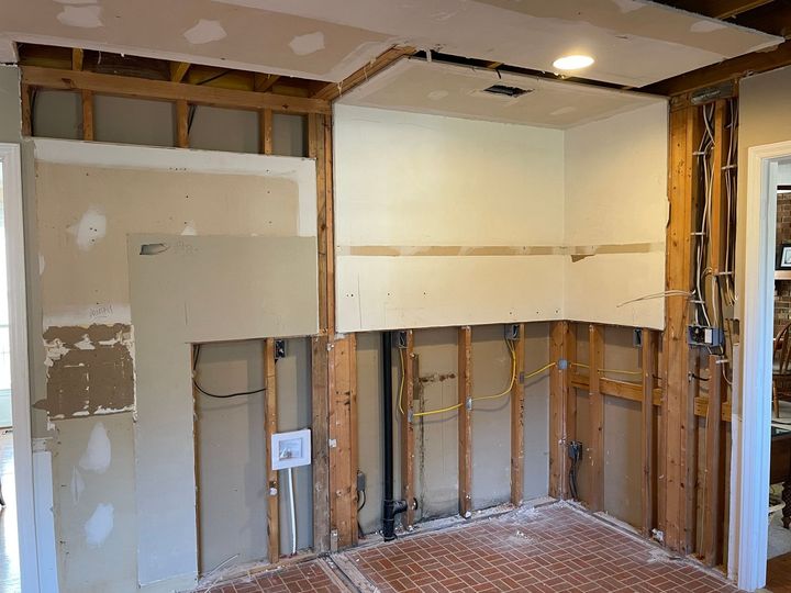 Kitchen wall under construction; exposed studs, partial drywall, electrical wiring visible.