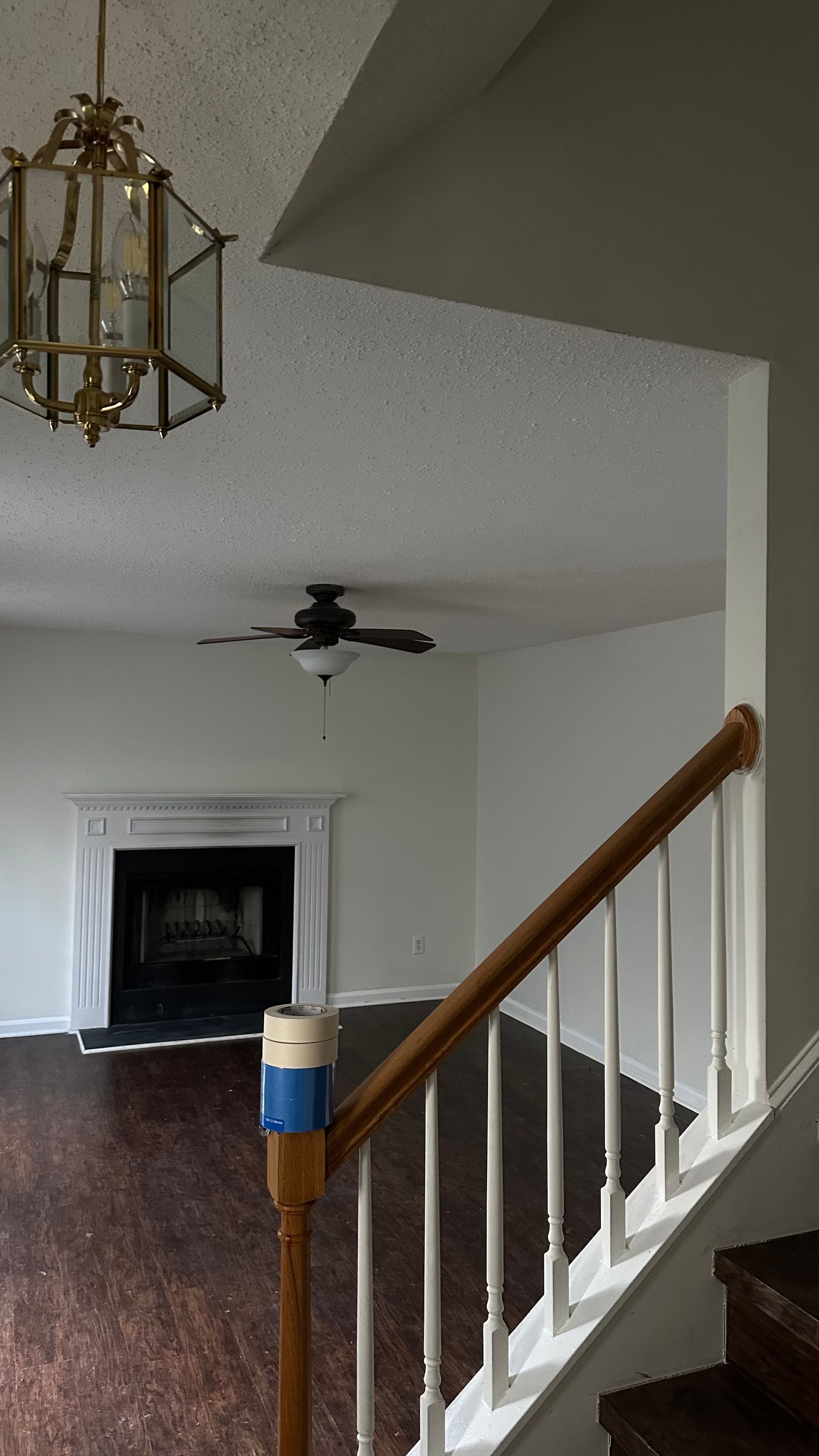 Staircase with dark wood steps and brown railing, leading to a living room with a fireplace and ceiling fan.