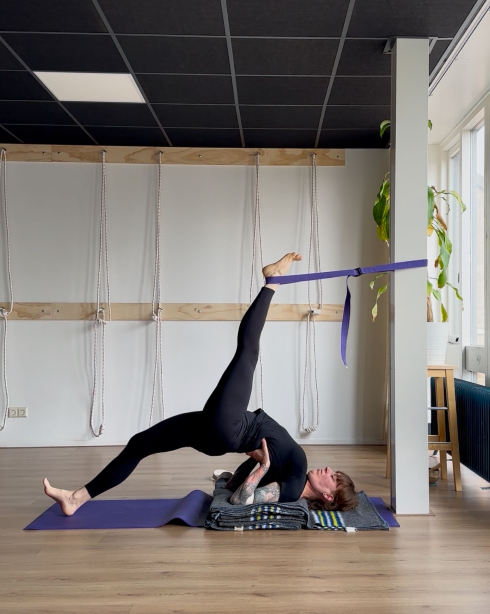 Eka pada setu bandha sarvangasana- backbend met precisie –een yoga riem en pilaar begeleiden de lift van het ene been. 