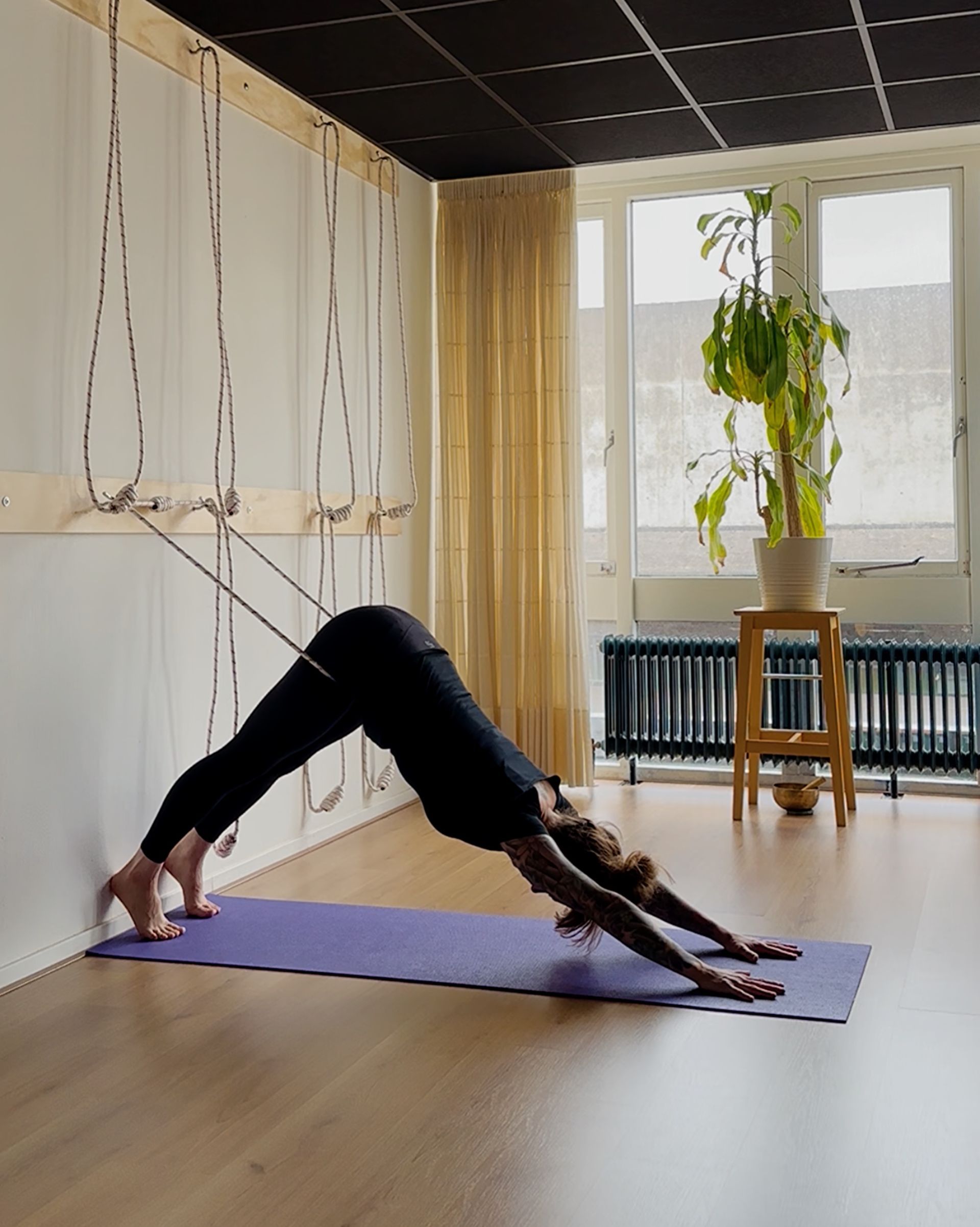 Adho mukha svanasana in de yoga touwen zorgt dat er geen belasting is voor polsen en handen.