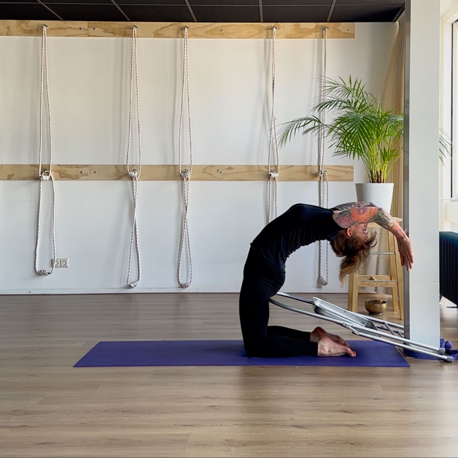 Ustrasana variatie met yogastoel tegen heiligbeen om bekken te tillen in backend