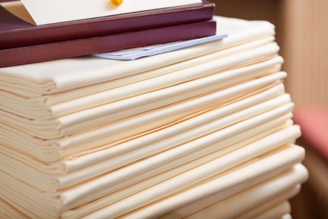 Stack of folded, cream-colored cloth napkins, topped with a maroon book and a card.
