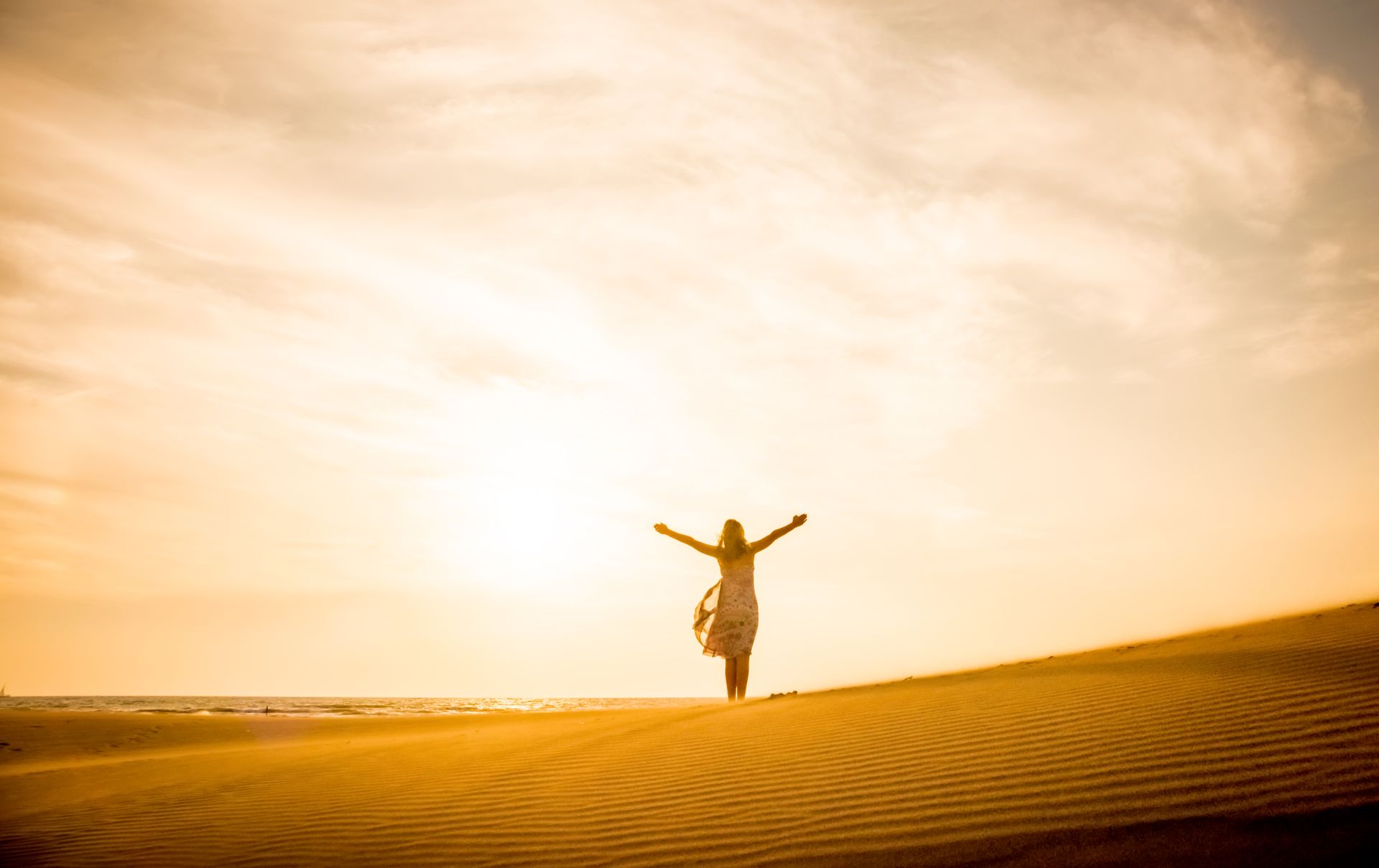 A woman is standing on top of a sand dune with her arms outstretched.