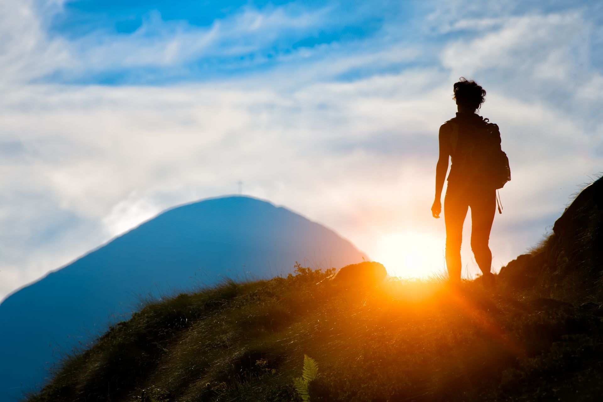 A man with a backpack is standing on top of a mountain at sunset.
