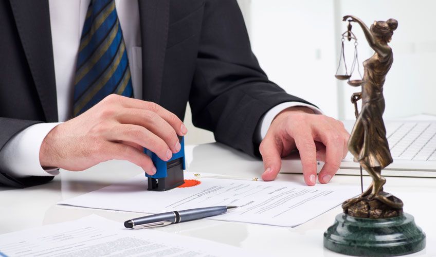 Un hombre está sellando un documento al lado de una estatua de la justicia.