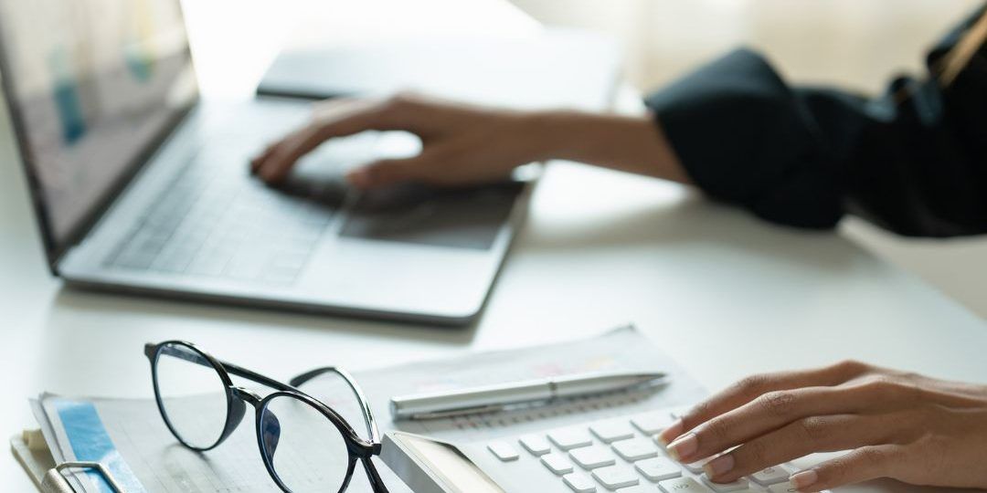 Una persona está escribiendo en una computadora portátil en un escritorio.