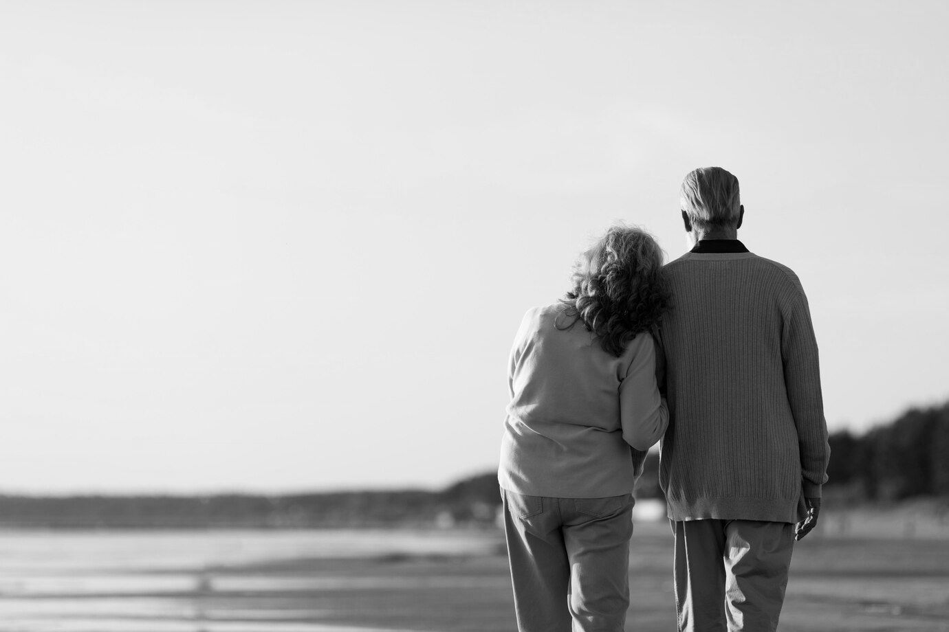 Una fotografía en blanco y negro de una pareja de ancianos caminando por la playa.