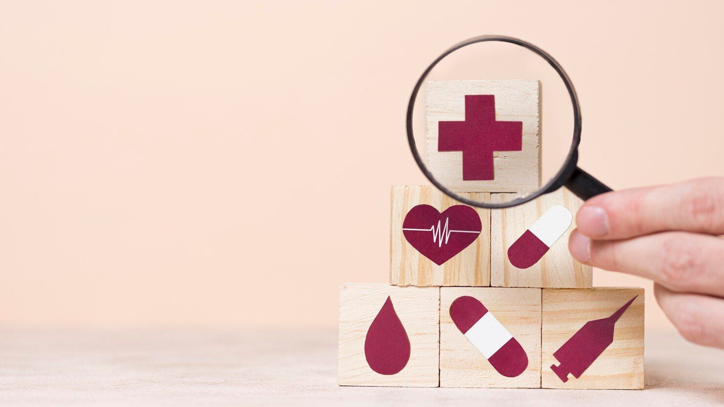 Una persona sostiene una lupa sobre una pila de bloques de madera con símbolos médicos en ellos.