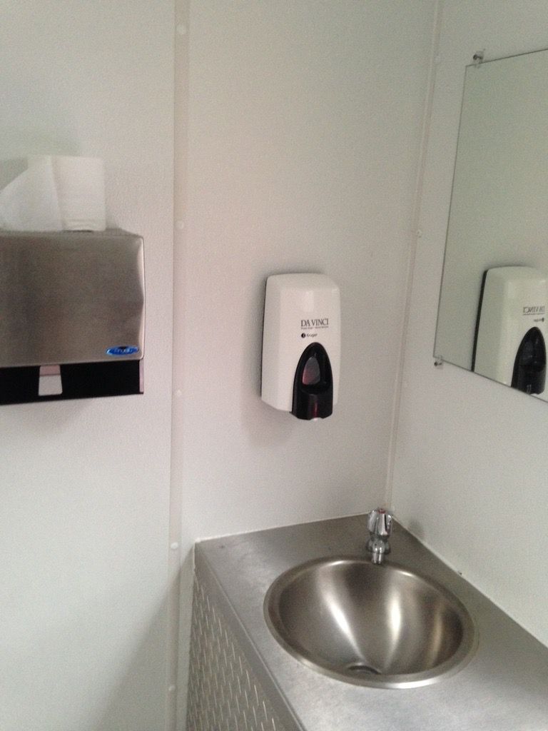 A bathroom with a sink , mirror and soap dispenser. Portable toilets. Brazeau Sanitation