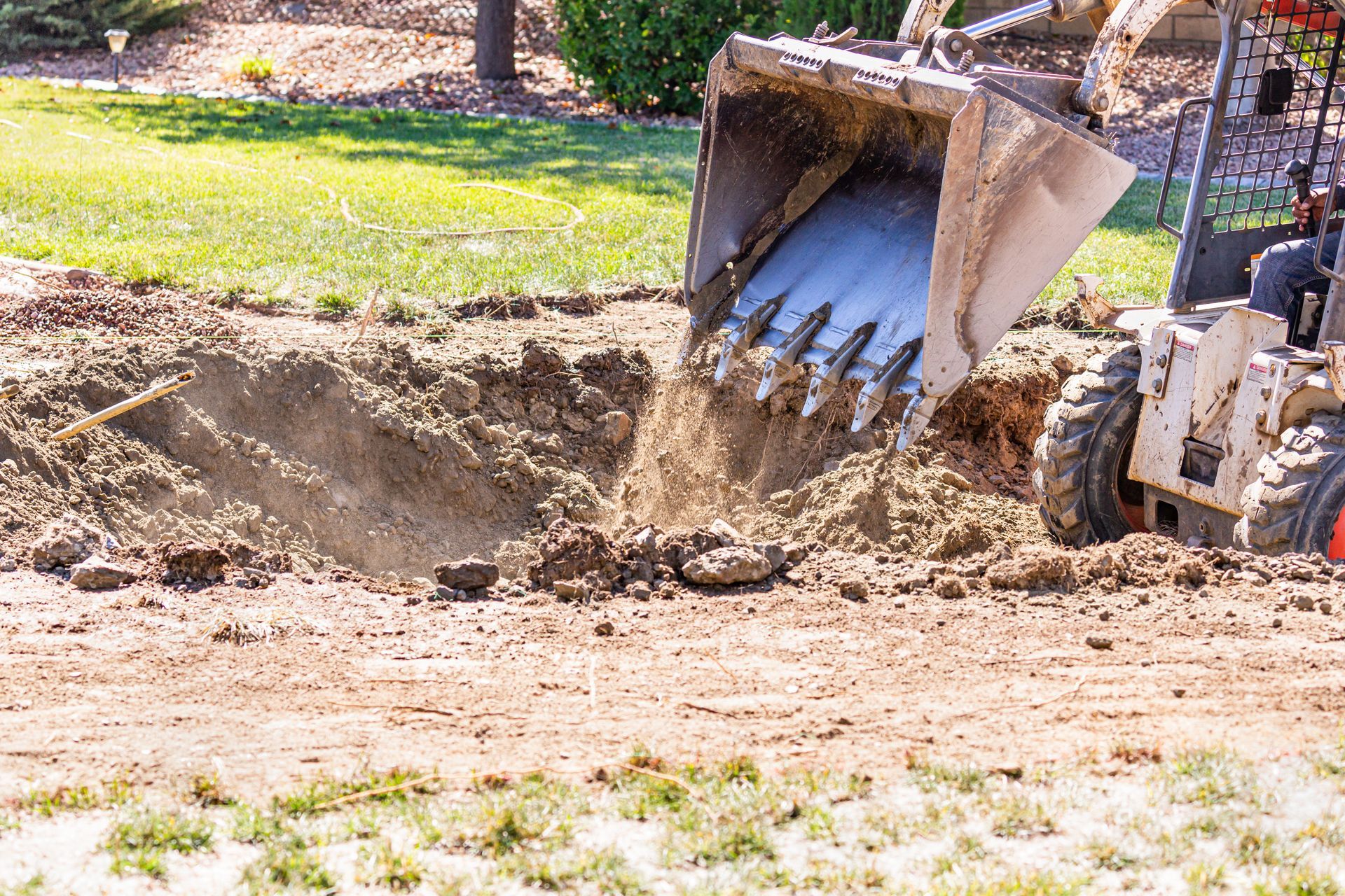 A yellow excavator is digging a hole in the ground in a park.