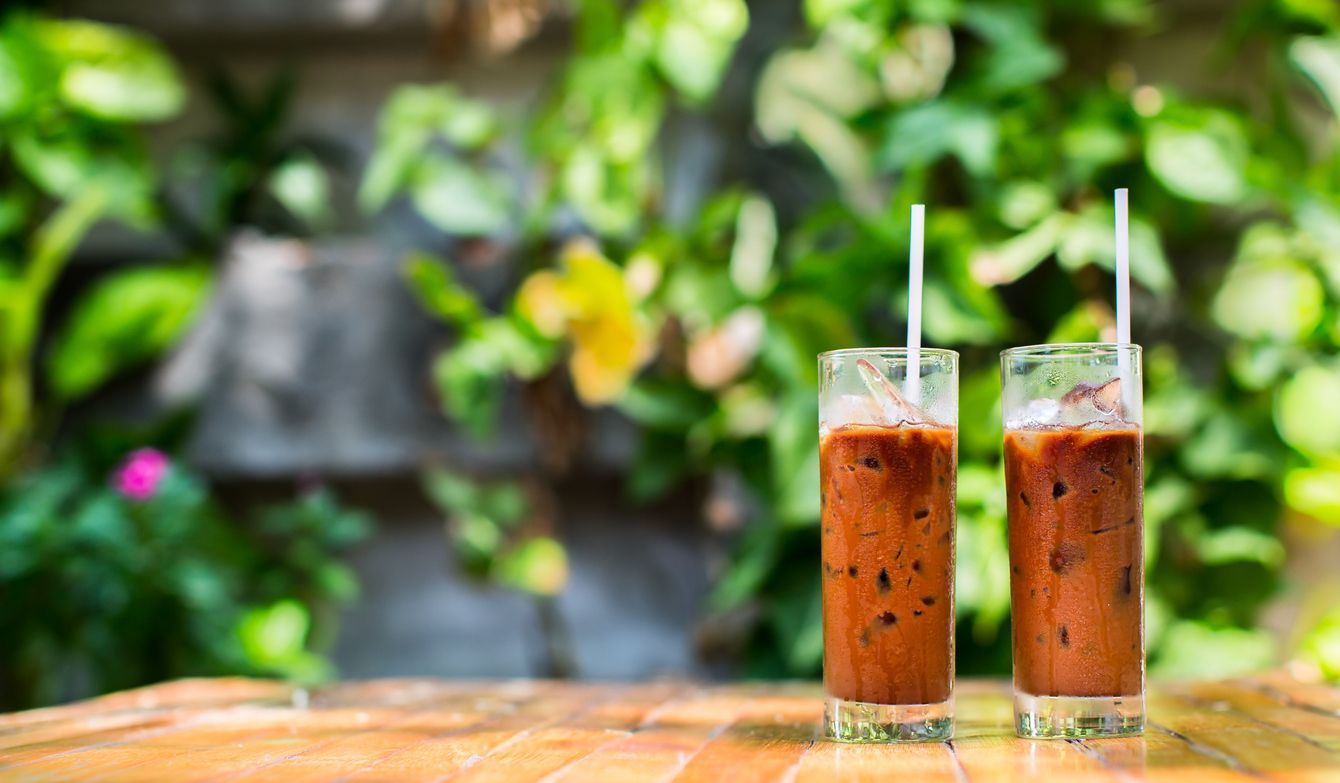 Two glasses of iced coffee with straws on a wooden table.