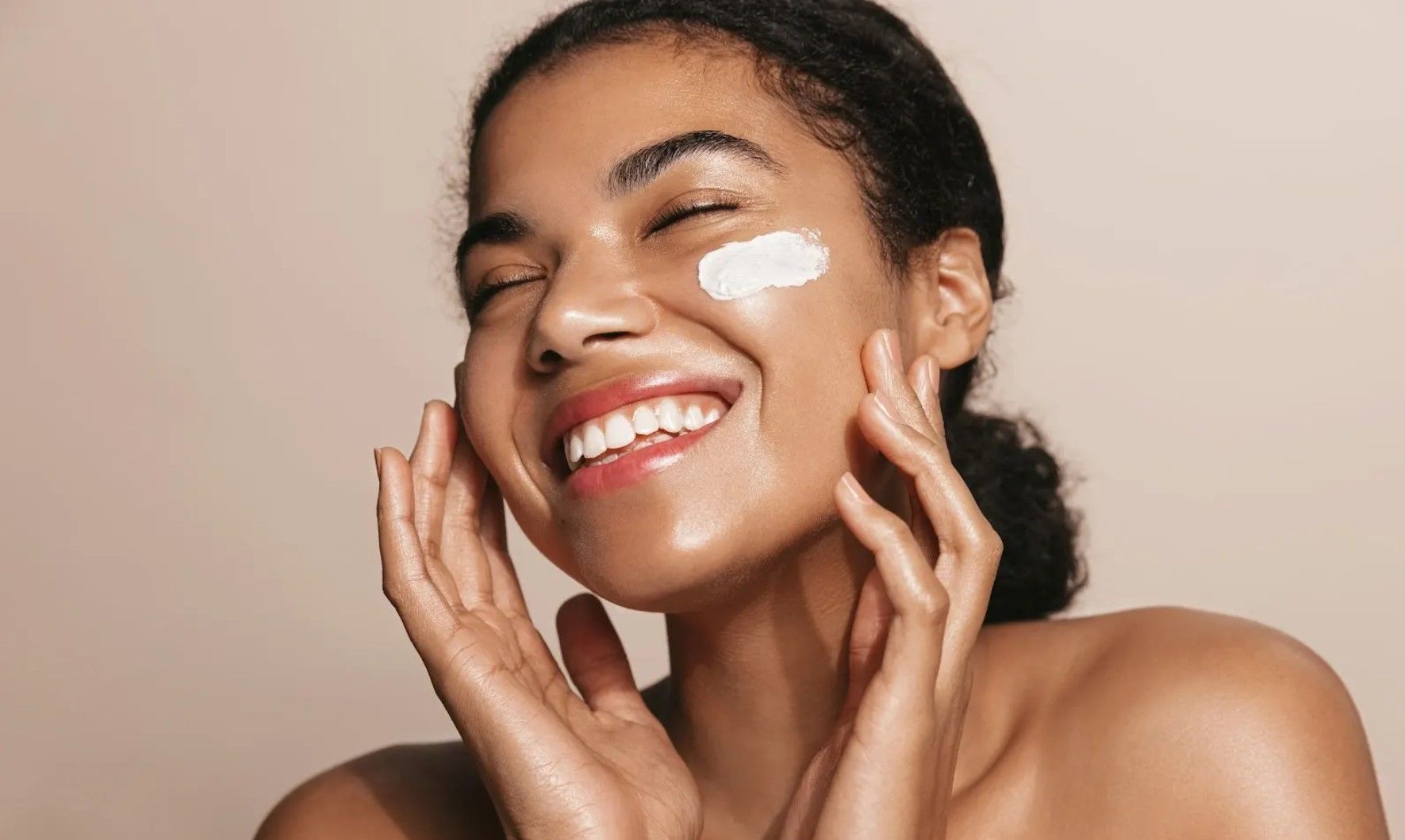 A woman is smiling while applying cream to her face.
