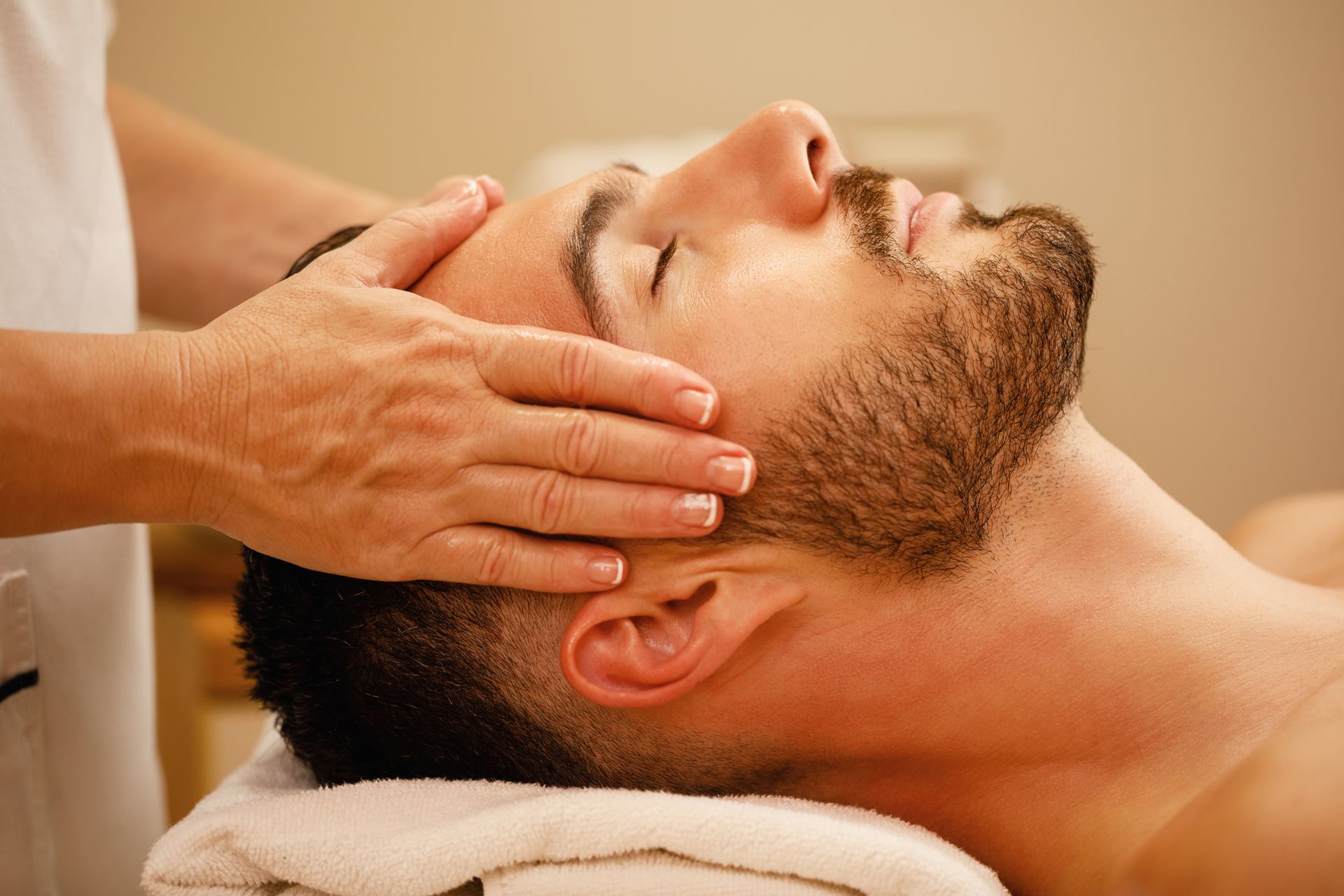 Man receiving a face massage. Therapist's hands on his forehead, relaxed expression, lying on a towel.