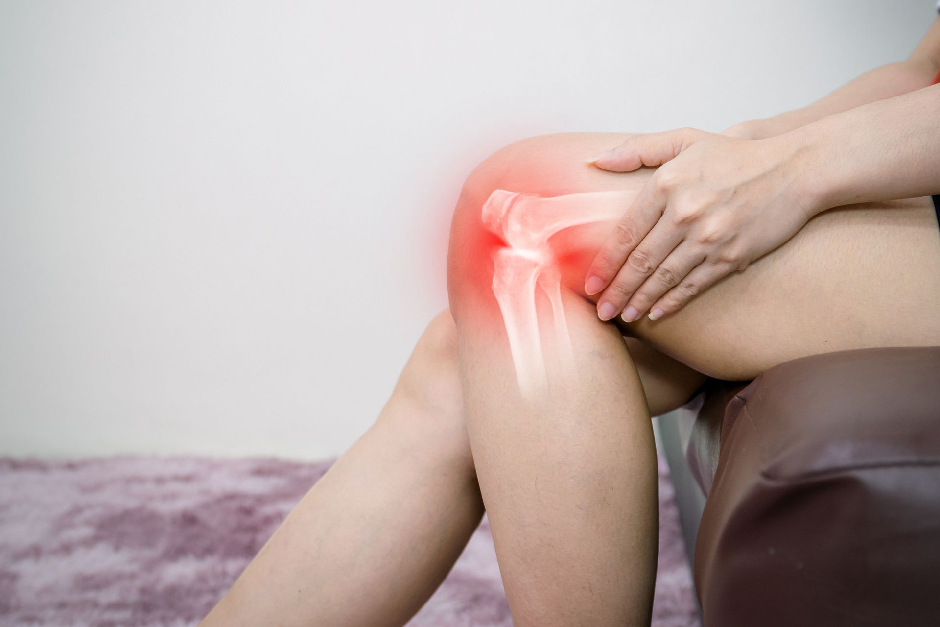 A woman is sitting on a couch holding her knee in pain.