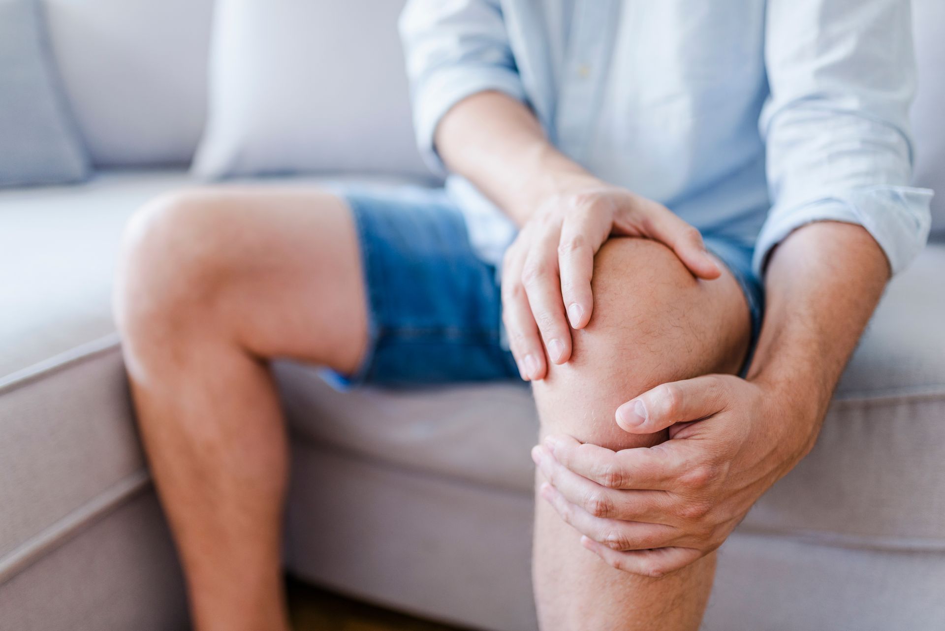 A man is sitting on a couch holding his knee in pain.